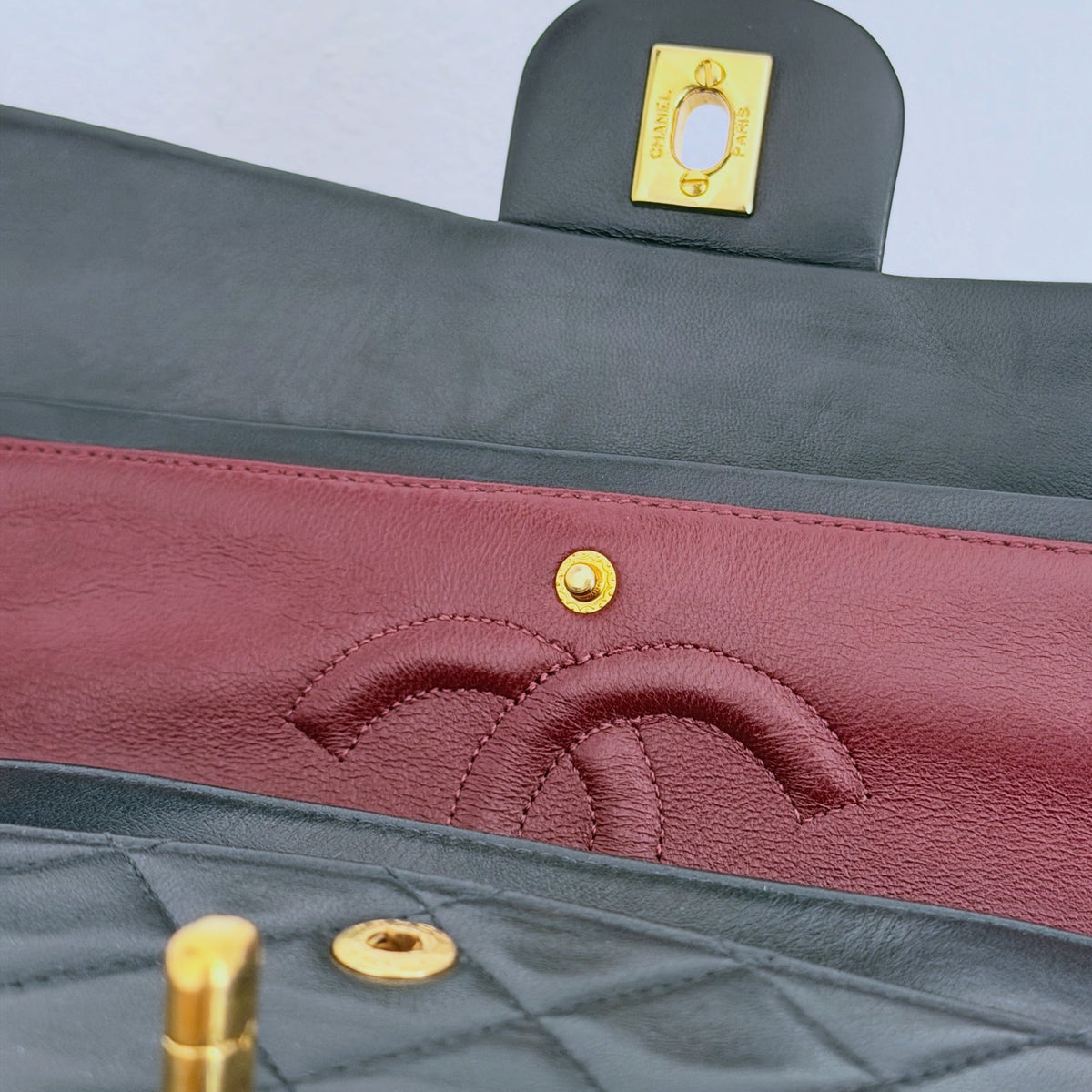 Detalhe interior da mala Chanel Classic Vintage Medium com pele preta, forro bordeaux e ferragens douradas 24K.